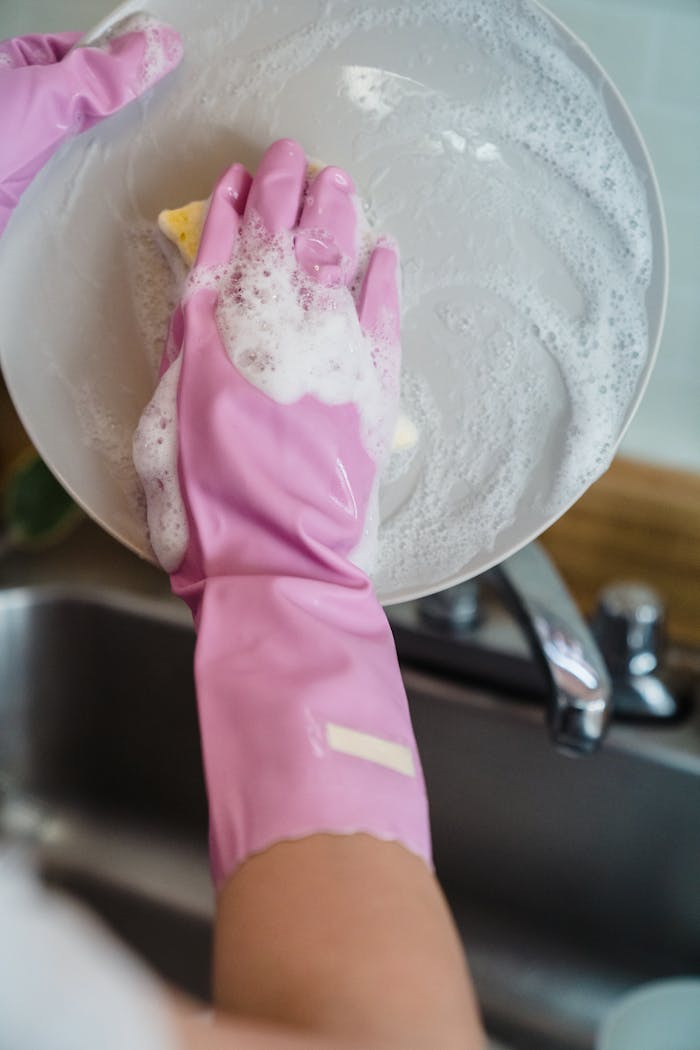 Close-up of hands in pink gloves washing a dish with soap suds for sparkling clean results.